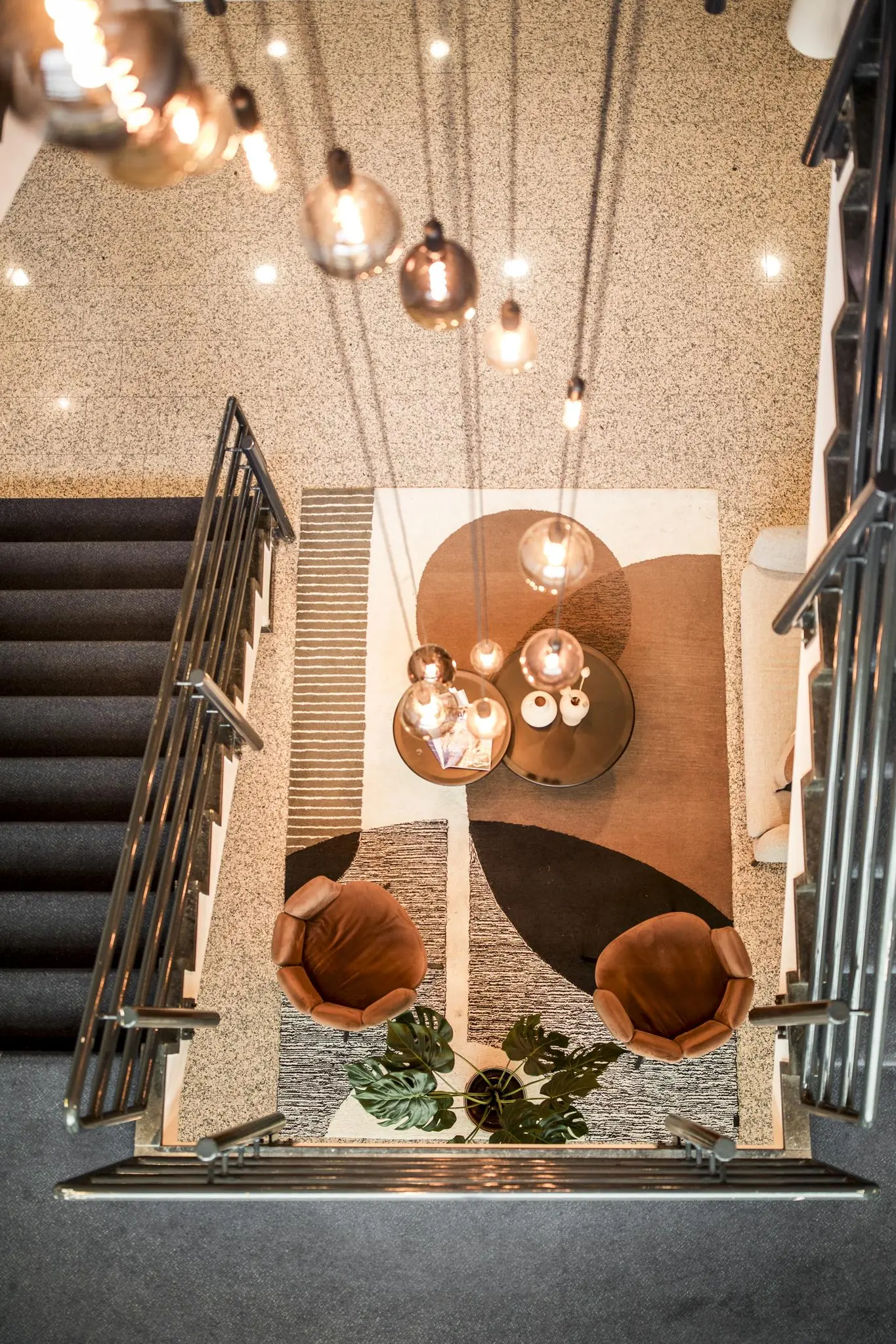 Bovenaanzicht van een modern ingerichte zithoek met twee bruine stoelen, een designkleed, hanglampen en een ronde salontafel in een trappenhuis aan de Markerkant 13.